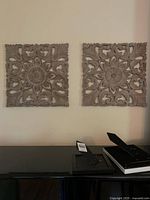 Pair of light brown reticulated natural wood square wall hangings displayed on a wall above a table