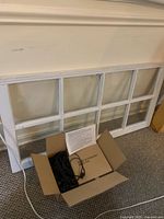 White wooden decorative window pane with six glass panels resting against the wall alongside an open box containing a coiled black string of globe lights and instruction paper.