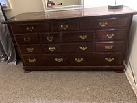 Front view of large solid wood dresser with brass handles, showing multiple drawers and dark brown finish