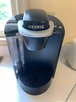 Front and angled view of black Keurig coffee maker with water reservoir, showing brand logo and control buttons.