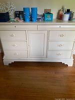 Front view of large cream-colored dresser with six drawers and central cabinet door, showing floral carvings on drawer fronts and cabinet door.