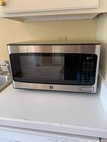 Front view of silver GE microwave oven on countertop showing digital keypad and display.