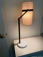 Modern lamp turned on showing the gray shade illuminated, black iron frame and circular marble base on a white surface.