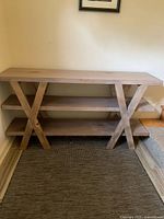 Full view of the modern wooden sofa table in light washed gray with three shelves and X-shaped legs.