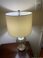 Full view of one lamp showing silver-speckled glass base and white drum shade, lit to display working condition.