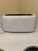 Front view of the Philips 2-slice toaster, white plastic body with Philips logo.