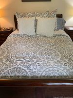Photo of the queen size bed made with a comforter featuring gray and white floral circular designs and five decorative pillows arranged at the headboard.