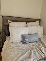 Full view of queen size bed with gray wood headboard and bedframe, dressed with several cushions and bedding.