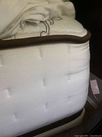 Close-up of the mattress side showing the white fabric with stitched holes and brown trim at the edges.