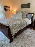 Side angle showing the headboard, footboard, and bedding on the dark wood sleigh bed frame, placed on a white shag rug.