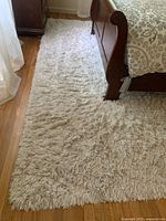 Photo showing rug alongside a bed and hardwood floor, displaying the texture and color of the cream shag area rug.
