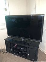 Full front view of Samsung flatscreen TV turned off on a black TV stand with doors and shelves.