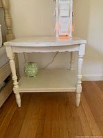 Front view of the cream colored bi-level side table showing spindle legs and bottom shelf