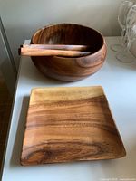 Photo of the set including the round wood salad bowl, wooden tongs inside it, and the square cutting board in front.