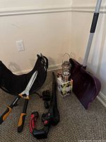 Lot arranged on carpeted floor showing a purple snow shovel, MZK blower with charger, Fiskars clippers, black fabric wood holder, and three copper lanterns stacked with box.
