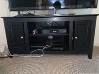 Image showing the entire black TV stand with electronic devices placed on the middle shelves and a TV on top.