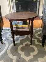Photo of the full table showing the round top, lower shelf, four turned legs, and overall structure on patterned rug.