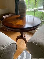 Full view of round wooden end table showing medallion wood pattern top and single central pedestal leg with three carved legs.