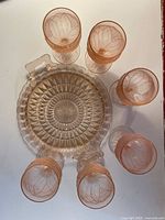Top view of 6 pink wine goblets arranged around a pink serving platter showing textured grapevine detail on goblets and diamond cut pattern on platter.