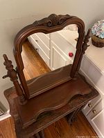 Front view of the antique dark wood vanity mirror showing curved wooden frame with carved Victorian details and side supports.