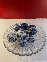 Top view of 7 blue and white porcelain decorative balls arranged inside a clear glass bowl with fluted edges.