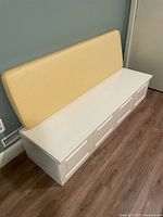 Full view of white wooden storage bench with yellow cushion on top, showing its size and appearance.