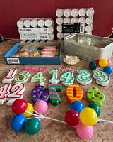 Set of colorful number candles, Happy Birthday toppers, IKEA GLIMMA tea lights in packages, assorted ball-shaped decorations, white rose candle, and metallic storage tin.