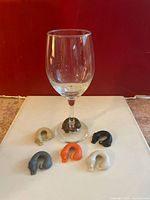 Clear wine glass with six dog-shaped silicone markers arranged around its base on a white surface in front of a red background.