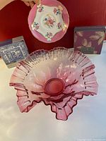 Top-down view of the cranberry glass bowl, two coaster boxes, and Aynsley saucer displayed on a white surface against a red background