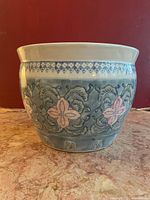 Front side view of the hand-painted porcelain pot showing blue and pink floral design on a light blue background.
