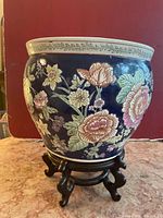 Exterior view of ceramic plant pot showing colorful floral patterns on a dark blue background placed on a wooden stand.