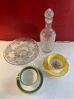 Photo of the lot showing decanter, clear glass embossed platter, yellow floral Foley teacup and saucer, and green & white Atlas teacup and saucer with gold trim.