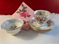 Photo of the teacup, four saucers stacked, one open sugar bowl, and 6 rose-design napkins showing floral patterns and gold trim.