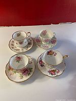Four vintage floral fine china teacups and saucers displayed together, showing varied floral patterns and gold trim.