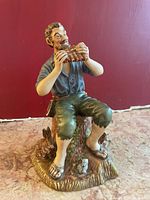 Front view showing man playing pan flute seated on tree stump, rabbit at base