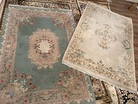 Two medium-sized floral area rugs shown together, one with blue-green background and beige border, the other with beige background and floral medallion center.