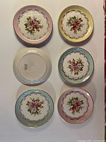 Top view of all six dessert plates arranged in two columns highlighting the floral pattern and gold-trimmed ornate border on pastel colored backgrounds.