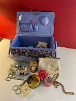 Open vintage floral sewing box showing thread spools, pincushion, small purse, scissors, and pins inside and in front