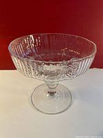 Clear crystal compote with textured ripple design on pedestal base against red background.