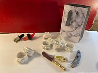 Full lot showing napkin rings, cheese cutters, wine stoppers, cork screw, and gift bag against red wall.