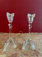 Two clear crystal candlestick holders with tulip-shaped tops, triangular bases, placed against a red wall on a countertop.