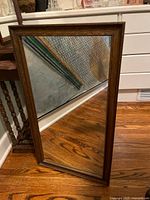 Full view of the antique traditional style rectangular mirror with brown solid wood frame, clear glass, standing on wooden floor.