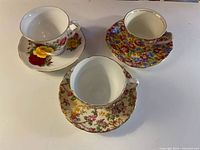 Set of three teacups with their matching saucers, each featuring different colorful floral bone china patterns with gold trim.