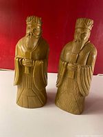Front view of two tan colored hand-carved stone bookends featuring Asian figures in robes with detailed facial features and hands clasped holding scrolls.