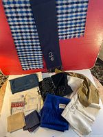 Photo showing the blue and white checkered scarf hanging, various scarves including navy and black with fringe, and multiple folded handkerchiefs in cream, tan, and blue with patterns