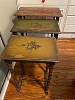 Front angled view of the nested tables showing floral painted surfaces and turned wooden legs