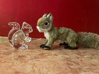 Two squirrel figurines side by side on marble surface against red background, showing scale and materials.