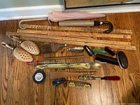 Top-down view showing wooden shoe stretchers, rulers, brushes, shoehorns, metal and plastic grooming tools, and two folded umbrellas lying on a wooden floor.