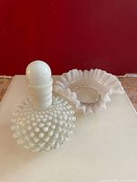 Photo showing the antique Wrisley cologne bottle with hobnail pattern and small bowl on a flat surface against a red background.