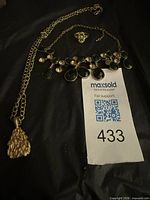 Overview of jewelry pieces laid out: bib necklace with green stones, nugget pendant necklace, small charm